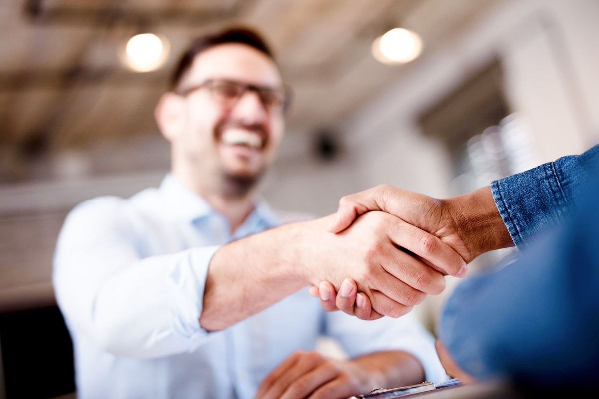 Zwei Personen geben sich die Hand, eine trägt ein blaues Hemd, die andere ein weißes Hemd.