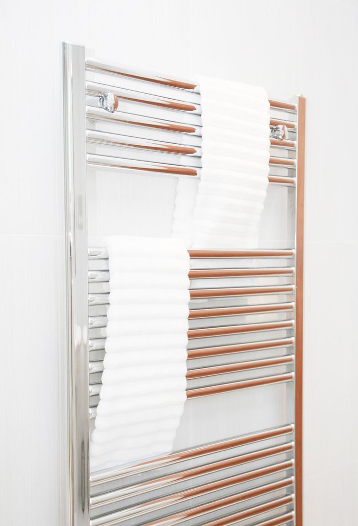 Chromfarbener Handtuchwärmer mit zwei weißen, geriffelten Handtüchern, an der Wand montiert.