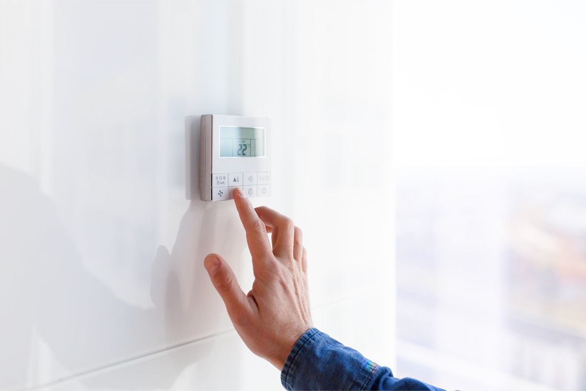 Hand in blauem Hemd bedient digitalen Thermostat an weißer Wand mit Display und Tasten.